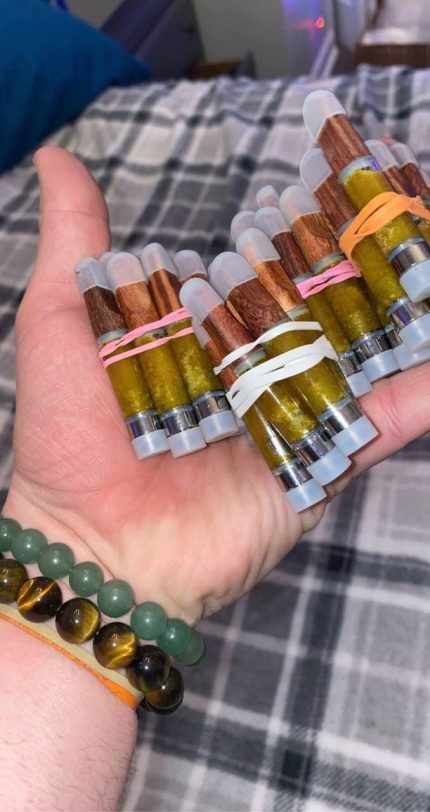 Hand holding bundled natural wood tip buy DMT cartridges 6-pack tanks showing golden crystalline extract