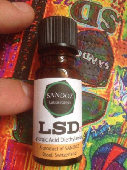 Amber glass bottle of Sandoz liquid LSD vial with a black cap and vintage Basel Switzerland label held over colorful artwork