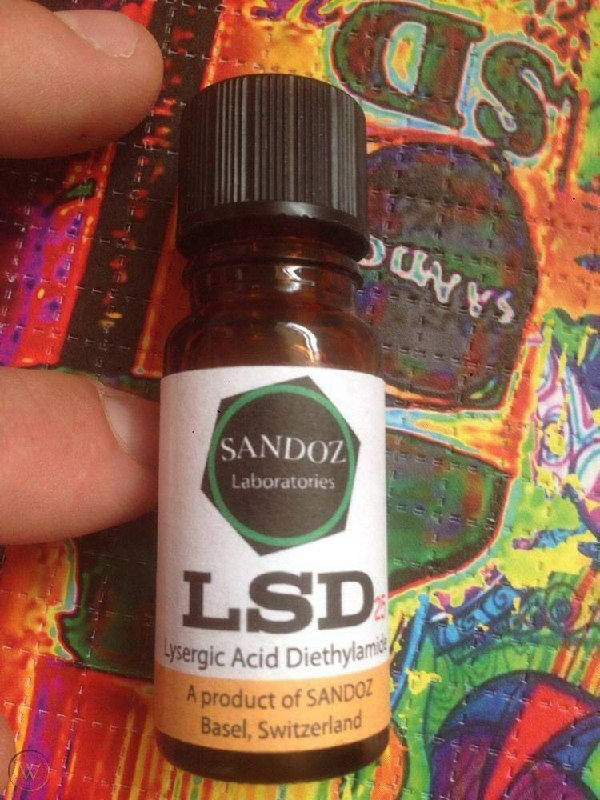 Amber glass bottle of Sandoz liquid LSD vial with a black cap and vintage Basel Switzerland label held over colorful artwork Amber glass bottle of Sandoz liquid LSD vial with a black cap and vintage Basel Switzerland label held over colorful artwork