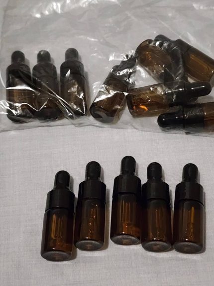 Multiple small amber glass pure liquid LSD vials with integrated pipette dropper caps arranged on a clean white surface